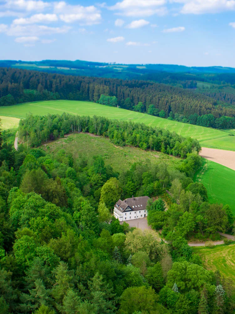 Die Tierarztpraxis Fernholte: ein Gebäude inmitten von Wald und Wiesen oberhalb von Attendorn, aus der Luft fotografiert.