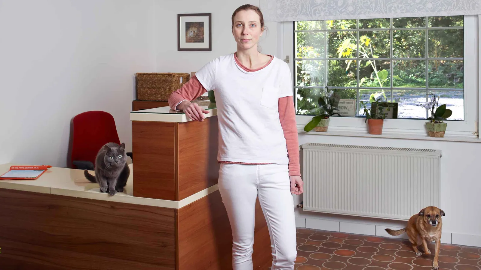 Dr. Magdala Köchling am Empfang der Tierarztpraxis Fernholte, daneben eine Katze auf dem Tresen und ein kleiner Hund.